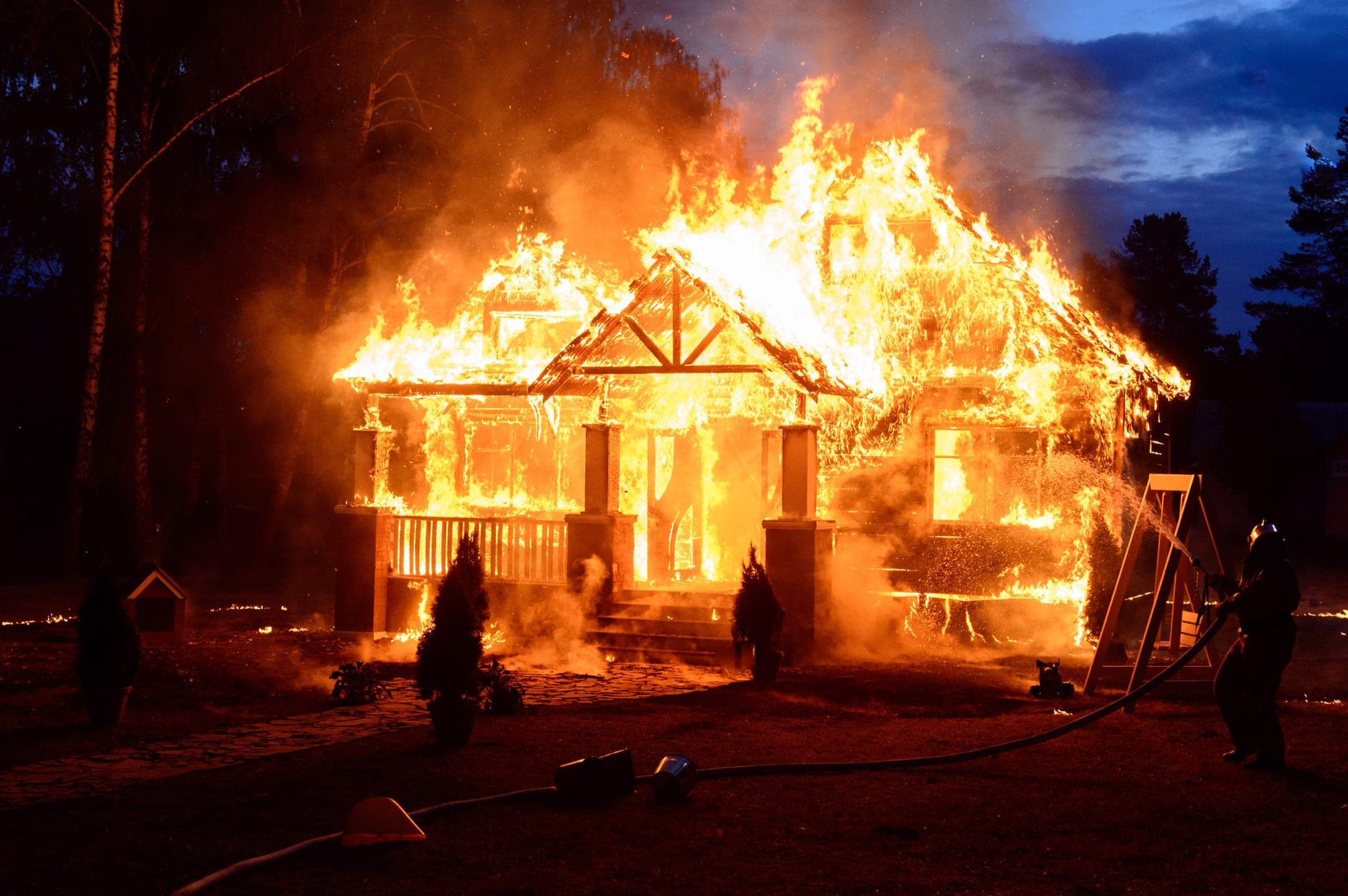Firefighter with a hose at a house fully engulfed at night